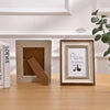 A wooden photo frame with a light gray border and a piece of natural wood inside, displayed on a wooden table.