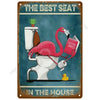 A vintage tin sign featuring a pink flamingo in a toilet, with the text The Best Seat in the House.
