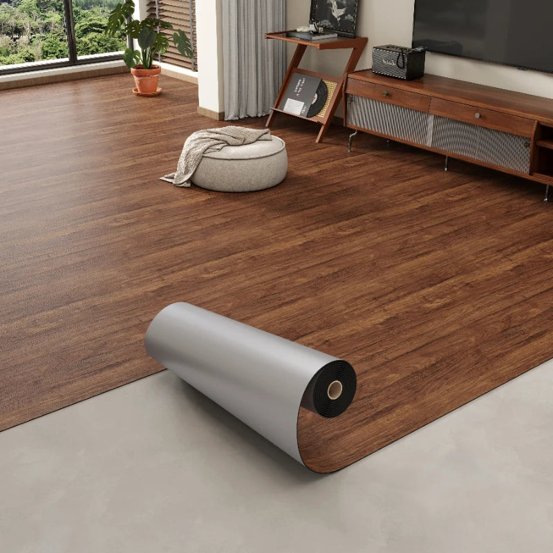 A roll of 3D textured wood grain self-adhesive flooring film placed on a light gray floor next to wooden furniture.