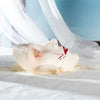 A pale pink ceramic masquerade mask with delicate silver and red accents rests on white fabric.
