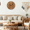 A living room features a minimalist wooden wall clock above a sofa and two wicker armchairs.