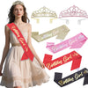A woman wearing a cream dress is positioned next to various gold, pink, and red birthday crowns and sashes.