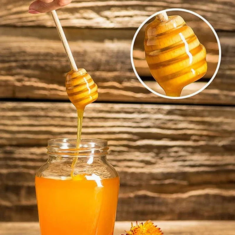 A honey dipper dripping golden honey into a glass jar, set against a wooden background.