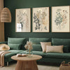 Three framed canvas prints featuring retro wildflower landscapes displayed on a dark green wall above a sofa.