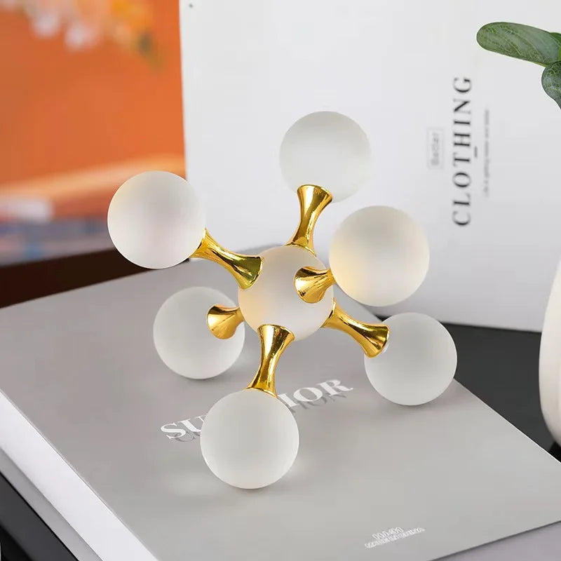 A minimalist molecular sculpture desk decor featuring gold and white spheres on a white surface.