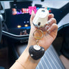 A hand holds a gold-toned keychain featuring a peach heart crystal charm and a silver locket.