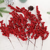 A cluster of artificial red holly berry stems used for Christmas decoration on a white fabric background.