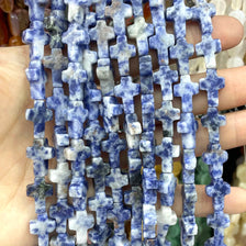 A string of natural stone cross beads in blue and white are held in a hand.