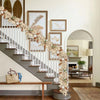 An artificial maple leaf garland draped along a staircase railing and wooden bench in a bright interior.