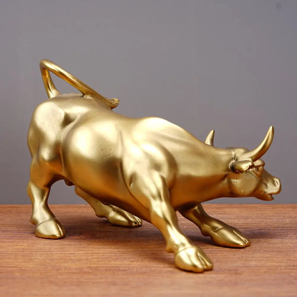 A golden sculpture of a bull in motion, displayed on a wooden surface.