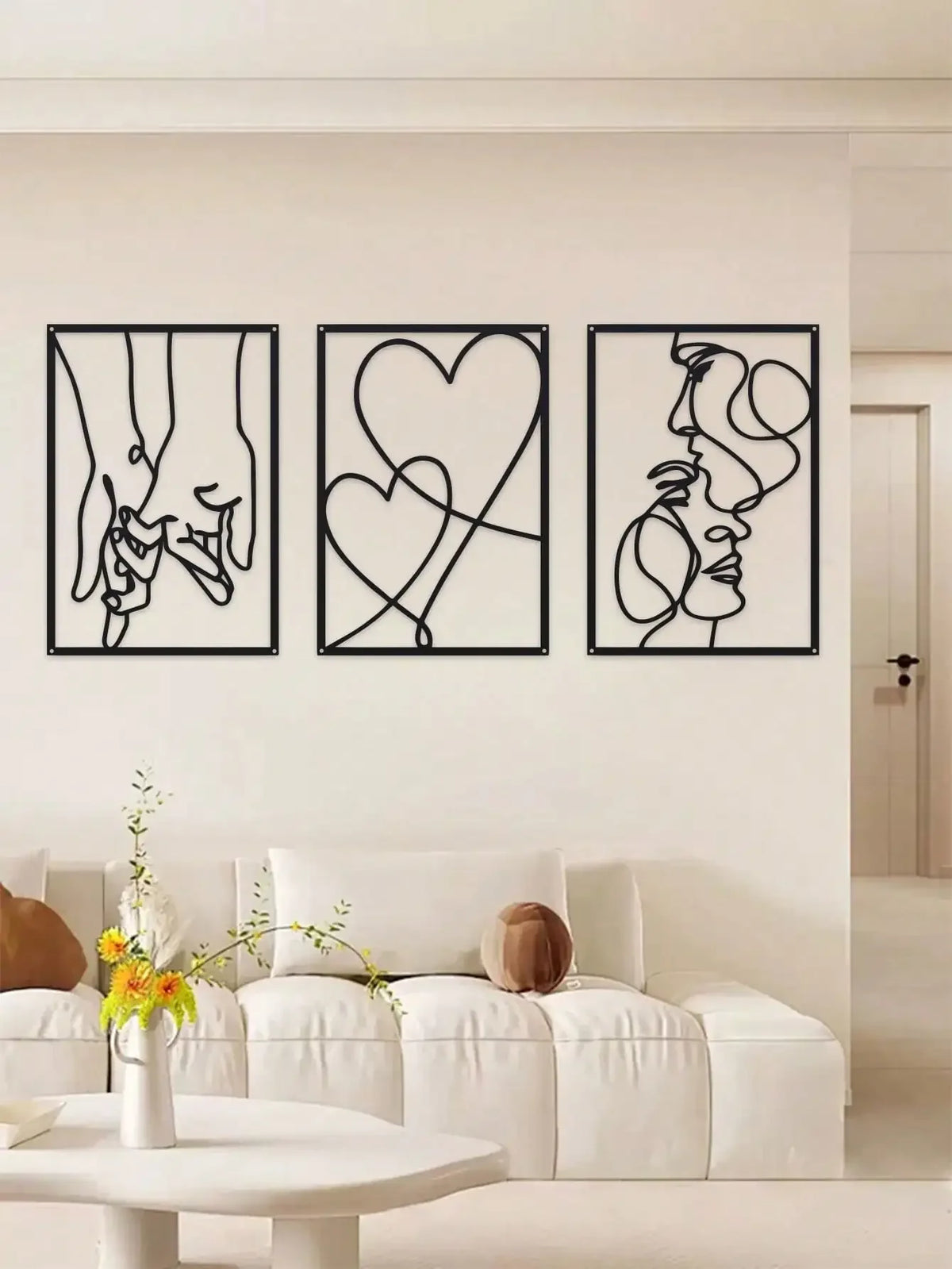 A set of three black line art prints depicting holding hands, a heart, and a profile face on white walls.