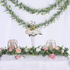 Une guirlande artificielle d'eucalyptus vert luxuriant drapée sur un fond blanc avec des accents floraux.