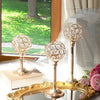 A set of three ornate crystal candle holders with a golden finish displayed on a table near a window.