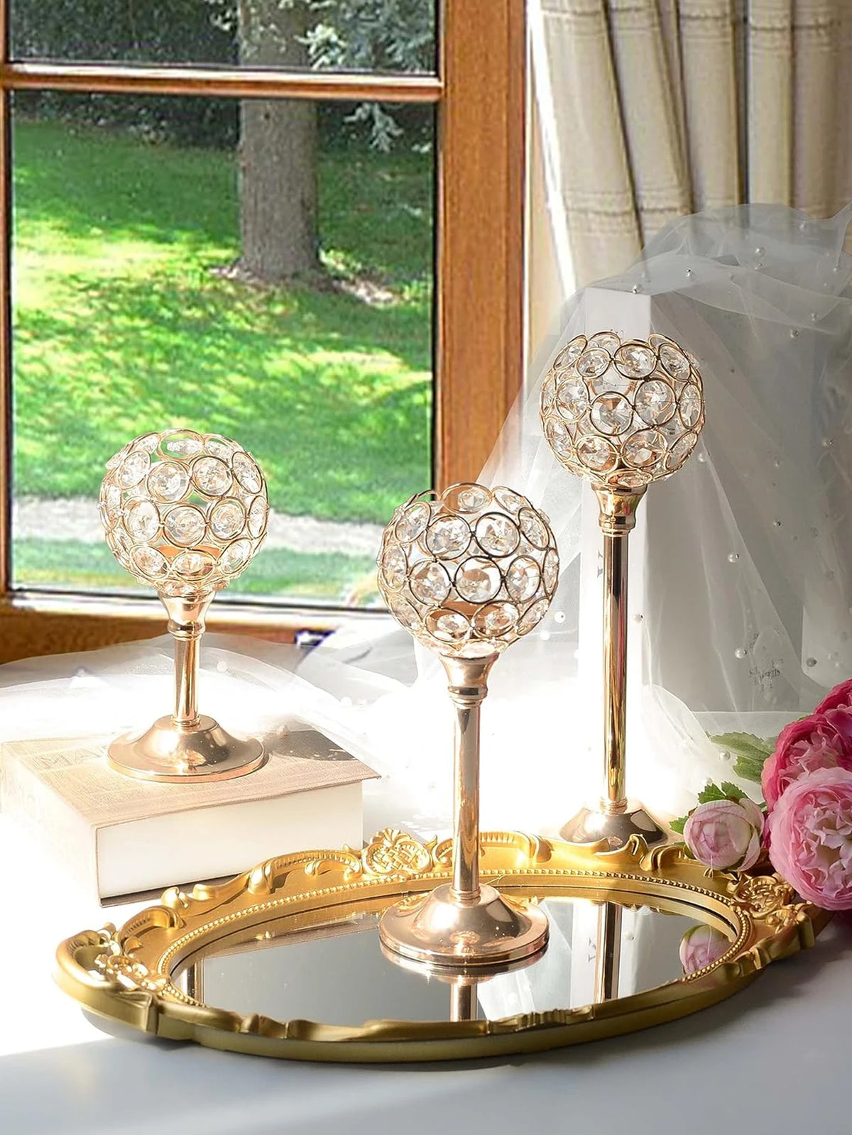 A set of three ornate crystal candle holders with a golden finish displayed on a table near a window.