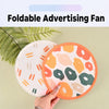 A hand is holding a colorful, foldable advertising fan with an orange border and floral pattern against a light green backgro