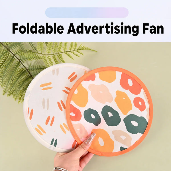 A hand is holding a colorful, foldable advertising fan with an orange border and floral pattern against a light green backgro
