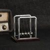 A silver Newton's cradle with glass balls rests on a dark surface next to a wooden box.