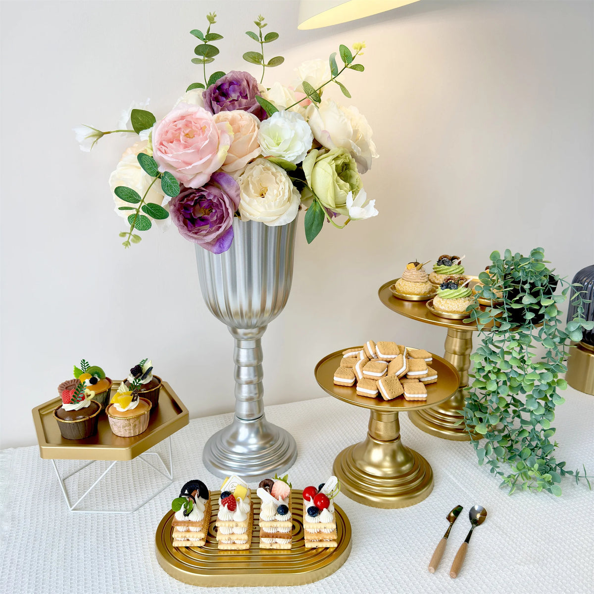 Elegant gold cylinder flower vases with mixed floral arrangements on a white tablecloth.