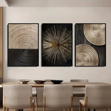 A set of three abstract canvas prints featuring concentric circle patterns in gold and black tones displayed on a light wall.