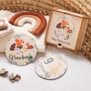 A set of wooden baby milestone cards featuring a newborn theme, displayed next to a wooden keepsake box and a cinnamon-colore