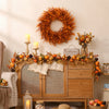 An artificial orange and brown eucalyptus wreath decorated with berries and foliage displayed on a wooden cabinet.