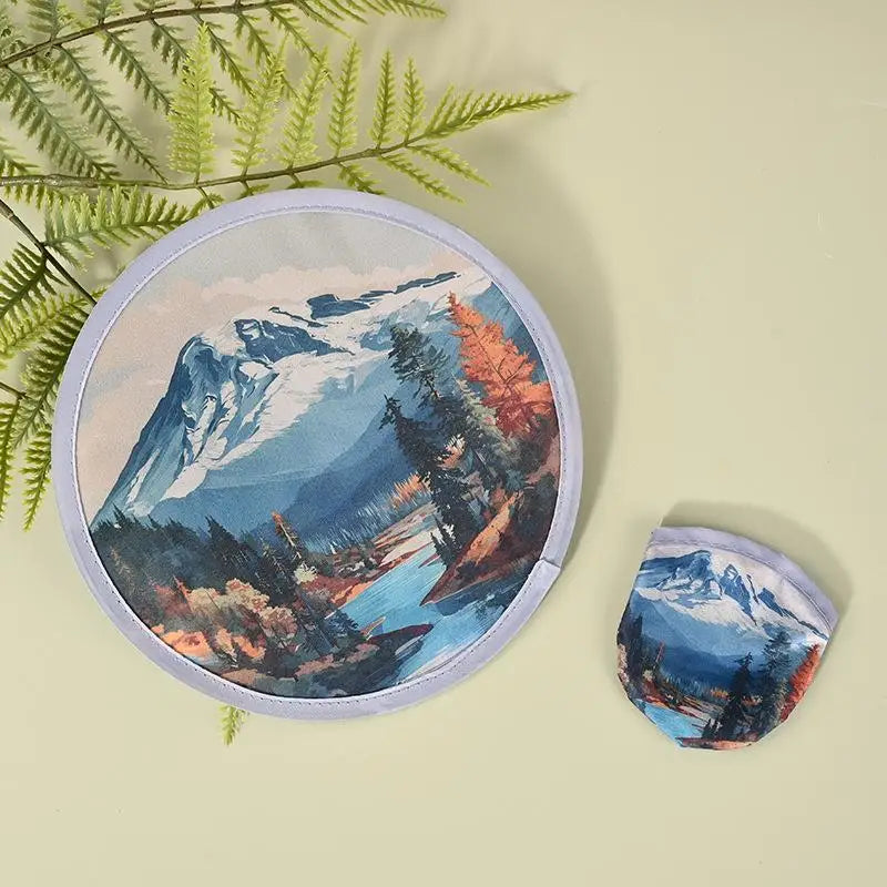 A round, purple fabric cooling fan depicting a mountain landscape with blue water and autumnal foliage.