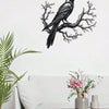 Black raven silhouette on a bare tree branch metal wall art displayed above a white sofa.