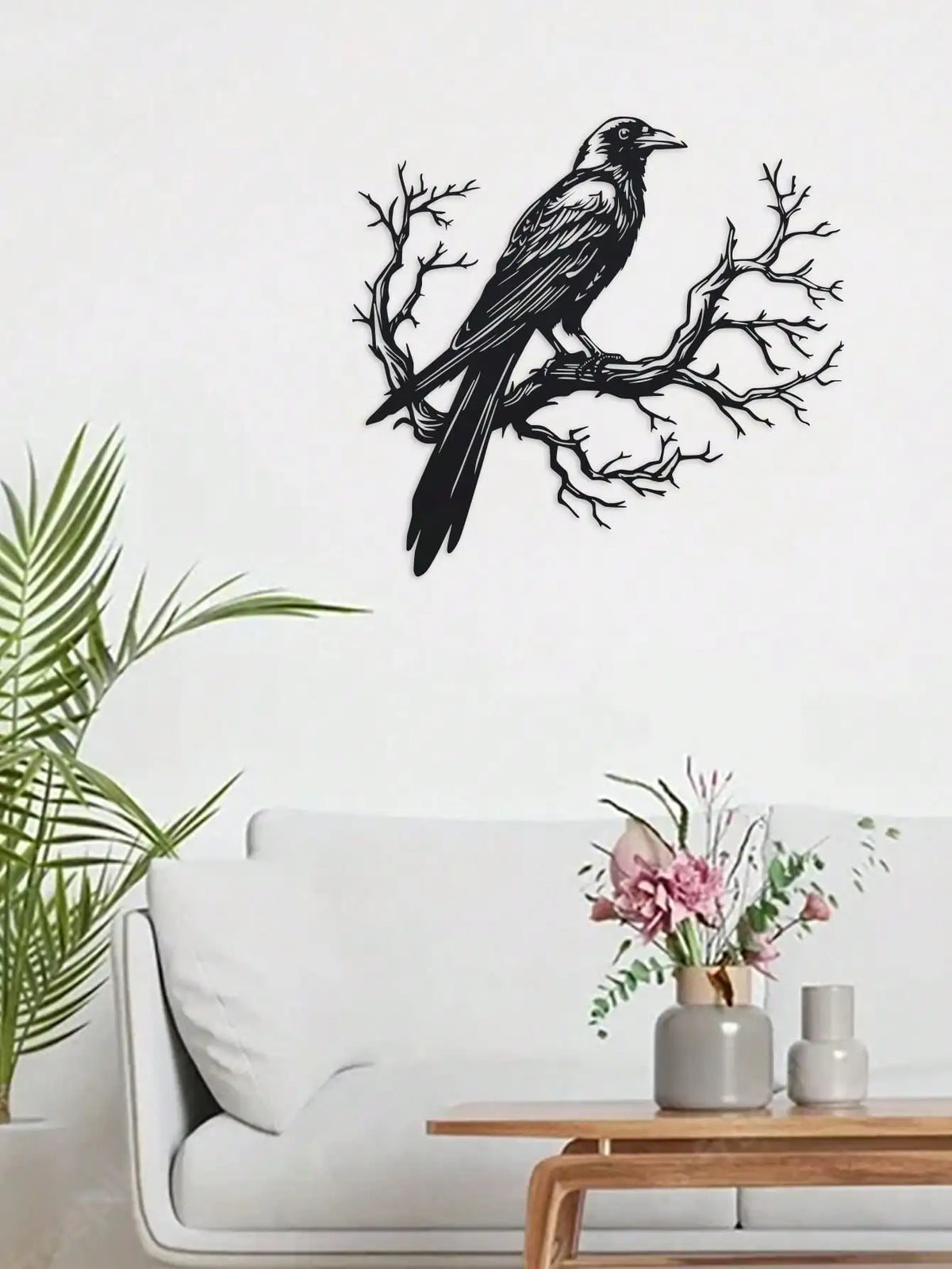 Black raven silhouette on a bare tree branch metal wall art displayed above a white sofa.