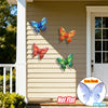 Four vibrant metal butterflies in blue, orange, and green are displayed on a light beige siding wall.
