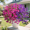 A large bouquet of vibrant purple and pink artificial silk flowers in a white vase set outdoors.