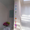 A silver crystal wind chime pendant featuring a rainbow of colored crystals hanging on a white wall.