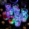 A collection of glowing LED light-up shot glasses arranged on a dark surface.