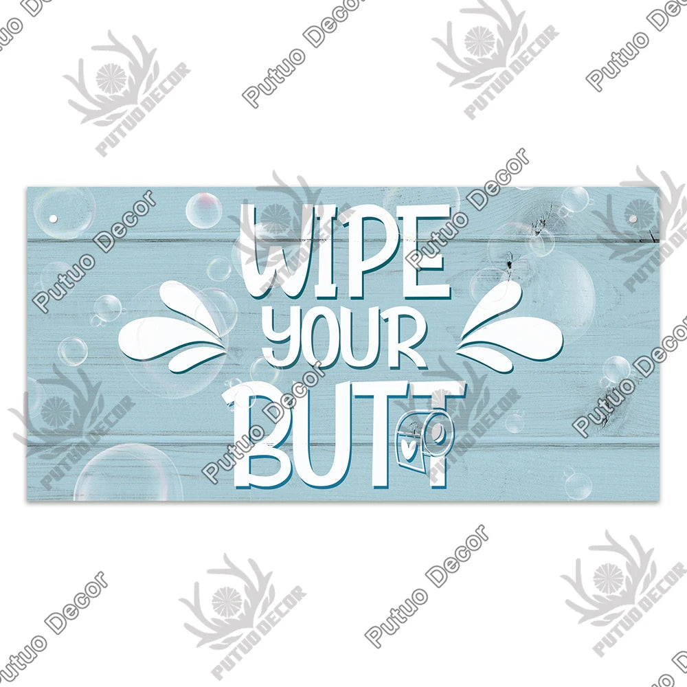A light blue wooden sign with white text instructing to wipe your butt.