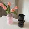 A pink glass flower vase holds several light pink tulips on a white countertop.