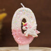 Una vela número cero blanca decorada con purpurina rosa y una pequeña figura de unicornio blanco.