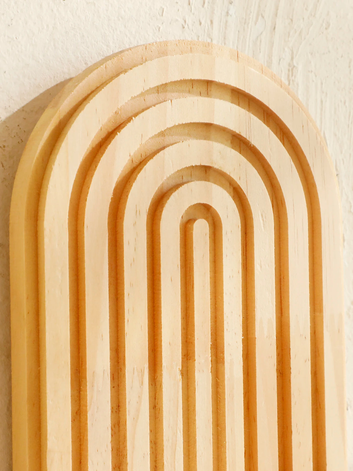 A close-up of geometric wooden wall shelves with parallel grooves and rounded arches.