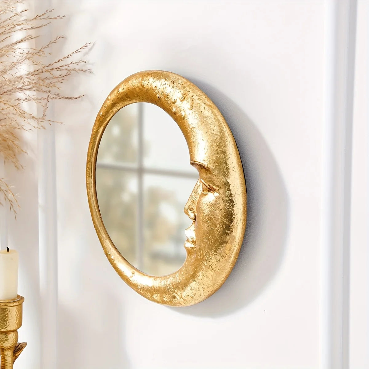 A round, gold resin decorative hanging mirror with an organic, crescent shape mounted on a white wall.