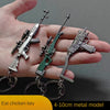 A hand holds a realistic miniature gun model keychain featuring an assault rifle and a pistol, made of metal.