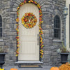 A cream-colored front door surrounded by a wreath of artificial autumn flowers and yellow foliage on a stone facade.