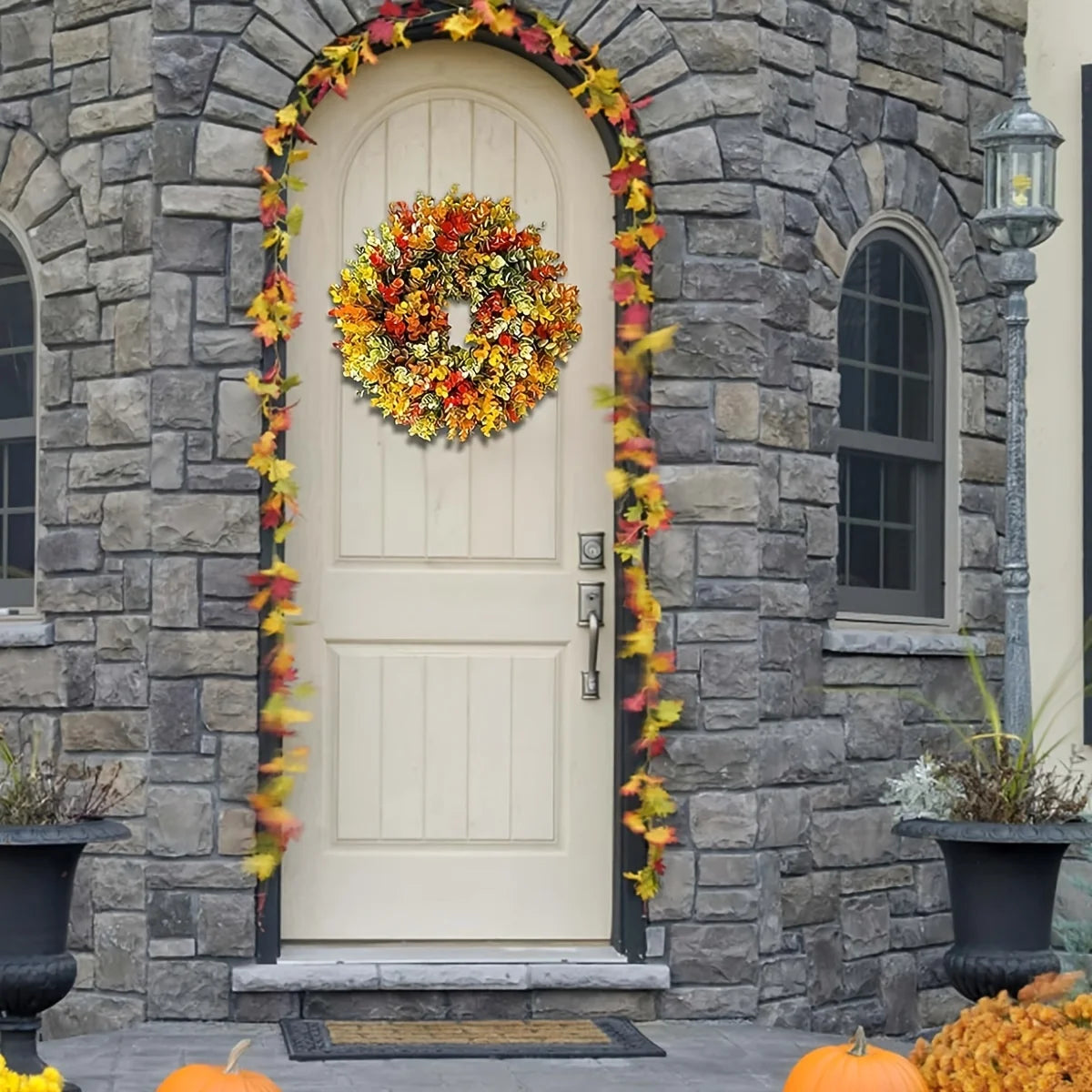 A cream-colored front door surrounded by a wreath of artificial autumn flowers and yellow foliage on a stone facade.