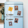 A light blue refrigerator decorated with several framed Halloween magnets featuring ghosts and pumpkins.