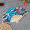 A hand carved bamboo folding fan with floral patterns displayed on a gray surface.