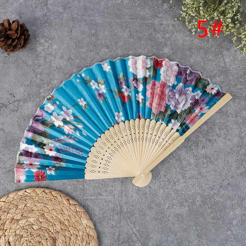 A hand carved bamboo folding fan with floral patterns displayed on a gray surface.