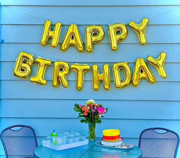 Gold foil letter balloons spelling HAPPY BIRTHDAY strung across a light blue wooden fence backdrop
