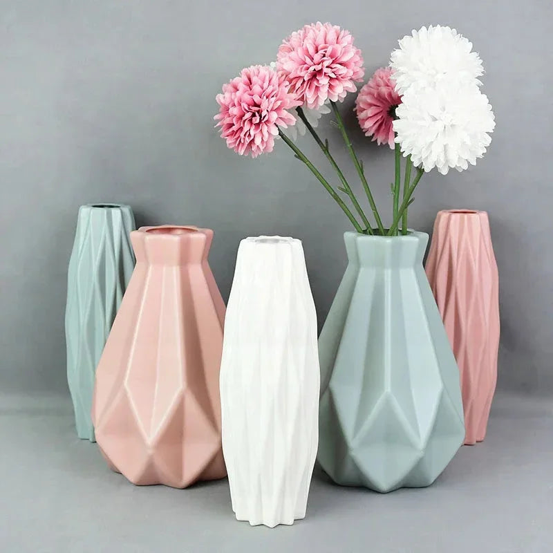 A collection of pink and white geometric plastic vases holding floral arrangements.