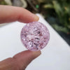 A hand holds a round, pink crystal ice crack ball water fountain decor.