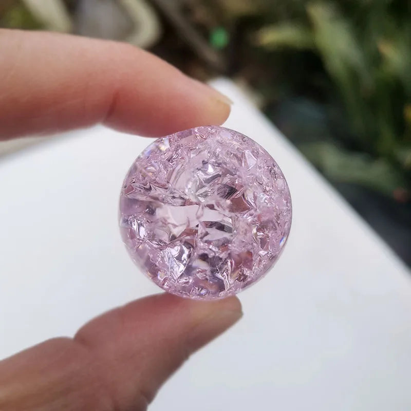 A hand holds a round, pink crystal ice crack ball water fountain decor.