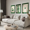 A modern living room features a light sofa, green accent walls, and framed art prints on the wall.