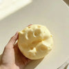 A hand holds a yellow, squishy cheese-shaped stress relief toy against a light background.