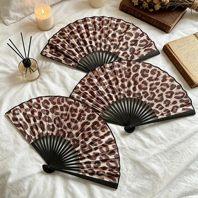 Nahaufnahme eines braun-schwarzen Leopardenmuster-faltbaren Handfans auf weißem Stoff.